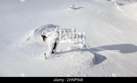 Jasna, Slowakei - 18. Januar 2018: Alte ungenutzte Skilifte fast vollständig mit Schneeladungen bedeckt, mit weißer Landschaft rund an sonnigen Wintertag. Beispiel für slowakische Skipisten. Stockfoto