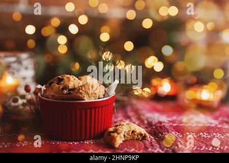 Rote festliche Schüssel voll mit leckeren Weihnachts-Schokoladenkeksen, verschwommener Hintergrund mit Weihnachtstanne Dekorationen, Lichter, Girlanden und Kerzen. Fe Stockfoto