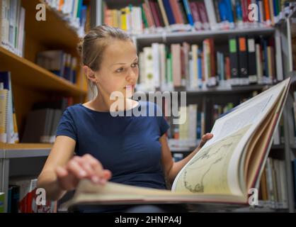 Hübsche, junge Frau, die ein altes Buch in Archiven zu studieren Stockfoto