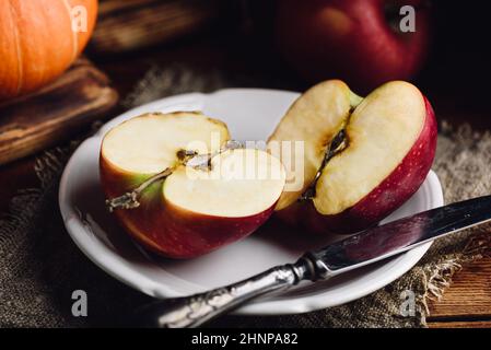 Zwei Hälften von rotem Apfel auf weißem Teller mit Vintage Messer in rustikaler Umgebung Stockfoto