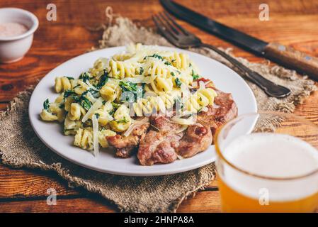 Gebratenes Schweinesteak und Spinat Pasta mit Ricotta und Parmesan Käse auf weißem Teller Stockfoto