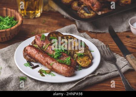 Gebackene Schweinswürste mit Auberginen und Lauch auf weißem Teller Garniert mit frischen Kräutern Stockfoto