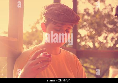 Der Junge sitzt auf einer Veranda und eatting frische Äpfel. Verträumt und romantisch Bild. Sommer und glückliche Kindheit Konzept Stockfoto