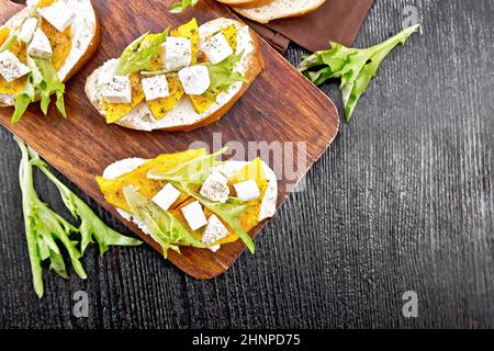 Bruschetta mit gebackenem Kürbis, gesalzenem Feta-Käse, Ricotta, Rucola und Gewürzen, Handtuch auf Holzbrett-Hintergrund von oben Stockfoto