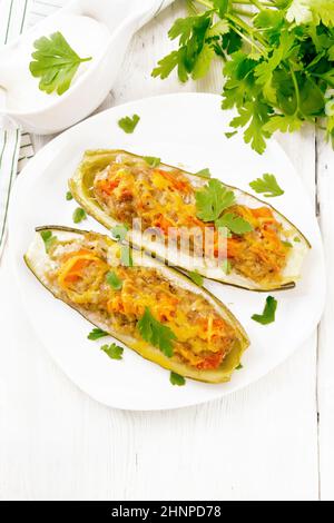 Gurken gefüllt mit Hackfleisch, Tomaten, Paprika mit Käse und Petersilie auf dem Teller, Rahm- und Grünsauce in einem Soßenboot, ein Handtuch auf Holzschwein Stockfoto