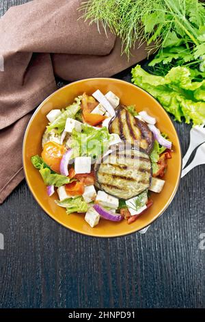 Salat aus gebratener Aubergine, frischer Tomate, Salat mit roten Zwiebeln und gesalzenem Feta-Käse, gewürzt mit Pflanzenöl und Sojasauce auf einem Teller, Handtuch, für Stockfoto