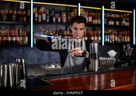 Barkeeper in der Schürze fügt dem Shaker Zutat hinzu Stockfoto