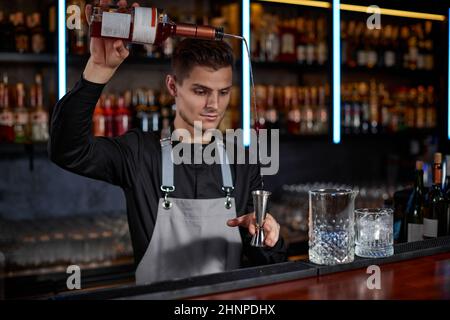 Barkeeper in der Schürze fügt dem Glas Zutaten hinzu Stockfoto