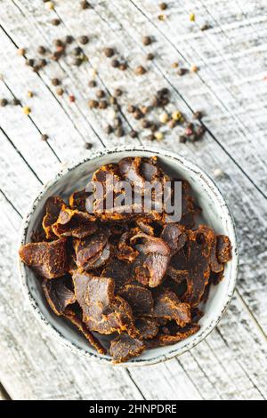 Rinderhackfleisch in Scheiben. Getrocknetes Rindfleisch in einer Schüssel auf einem Holztisch. Draufsicht. Stockfoto