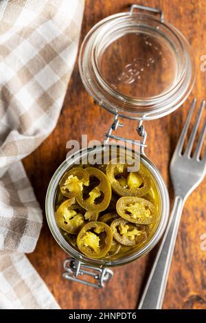 Eingelegtes Jalapeno in Scheiben. Grüne jalapeno Paprika im Glas auf Holztisch. Draufsicht. Stockfoto