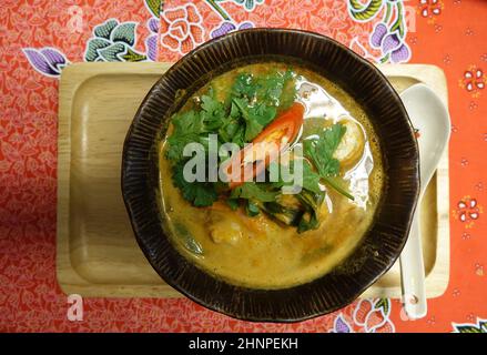 Braune Bambusschüssel mit heißer und köstlicher hausgemachter traditioneller Tom Kha Gai Suppe auf roter Tischdecke, Bangkok, Thailand Stockfoto