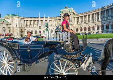 Die Menschen fahren in der Pferdekutsche namens Fiaker und vorbei an der Wiener Hofburg Stockfoto