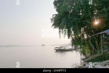 Horizont über dem Fluss gegen klaren Himmel im Hintergrund und Baum im Vordergrund des Flussufers. Blick auf die Landschaft am Ganges-Fluss während des Sonnenuntergangs. Budge Budge Stockfoto