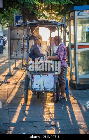 Die Frau in einem tragbaren Imbisswagen bietet auf der Straße in Bangkok frisch gegrillte Hühnersticks an Stockfoto