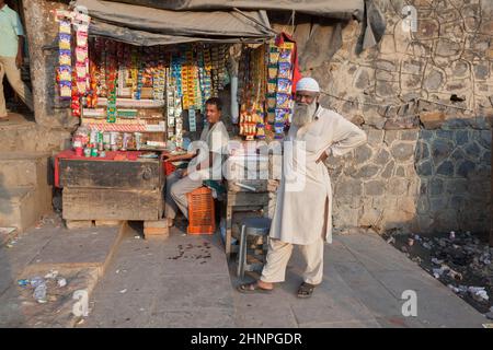 Ein älterer Mann steht vor einem Kiosk im Bereich des Meena Bazaar in Alt-Delhi, während sich der Besitzer des Kiosk in der Mittagshitze entspannt Stockfoto