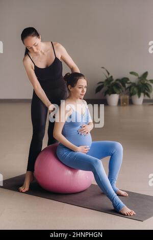 Eine Schwangerin mit einem Trainer während des Fitnesskursen mit einem Ball Stockfoto