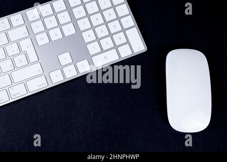 Draufsicht auf weiße und silberne Tastatur und Maus auf schwarzem Hintergrund. Stockfoto