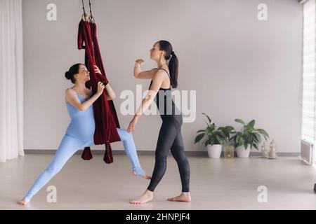 Schwanger. Eine Frau mit Trainer macht Yoga in einer Hängematte im Fitnessstudio. Das Konzept eines gesunden Lebensstils, Mutterschaft Stockfoto