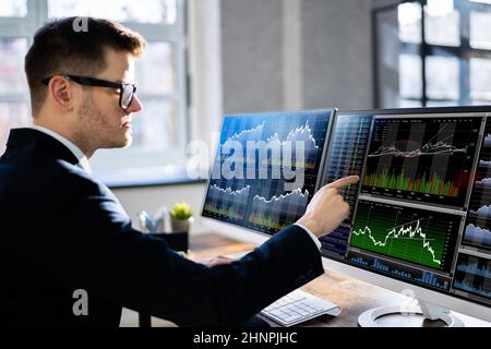 Junge Männliche Börsenmaklerin, Die Sich Die Grafik Am Computer Am Arbeitsplatz Ansieht Stockfoto