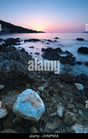 Blick auf das Meer bei Sonnenuntergang mit kristallklarem Wasser und Felsen und Steinen im Vordergrund Stockfoto