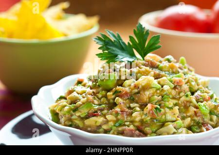 Guacamole-Salat in Schüssel weiß mit Petersilie obenauf angeordnet Stockfoto