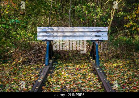 Puffers am Ende einer verlassenen Bahnlinie bei strahlendem Wintersonnenschein, mit gefallenen Blättern, die die Schwellen zwischen den Gleisen bedecken. Stockfoto