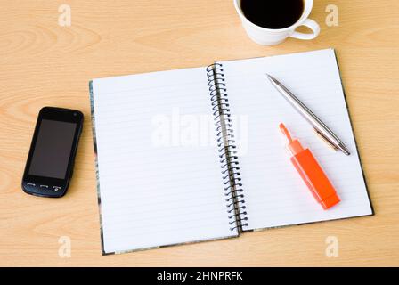 Mobiltelefon mit Spiralnotizbuch und einer Tasse Kaffee auf dem Bürotisch Stockfoto