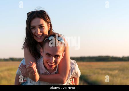 Junger Mann, Freundin auf seinem Rücken zu tragen und Spaß in der untergehenden Sonne Stockfoto