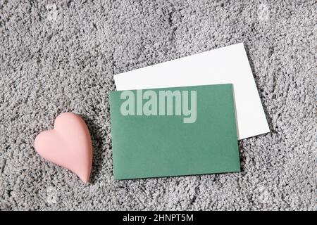 Grußkarte zum Valentinstag. Weiße und grüne Umschläge, Keramik rosa Herz auf einem grauen flauschigen Teppich Hintergrund. Speicherplatz kopieren. Für Text platzieren Stockfoto