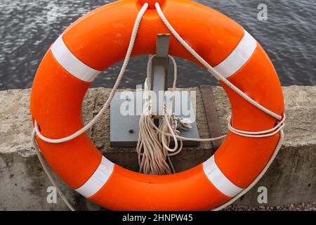 Orangefarbene Rettungsboje mit Seil, das an einem Steg in der Nähe des Wassers hängt Stockfoto