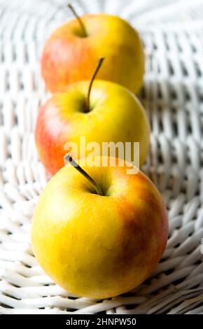 Drei frische Äpfel auf einem weißen alten Korb angeordnet Stockfoto