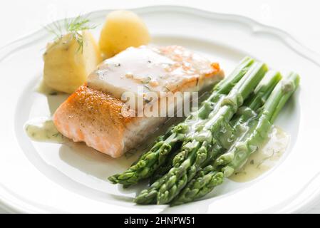 Nahaufnahme von gegrilltes Lachsfilet mit Kartoffeln und Spargel garniert mit Dillsauce auf weiße Platte angeordnet Stockfoto