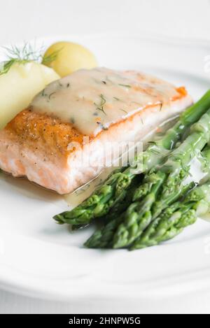 Nahaufnahme von gegrilltes Lachsfilet mit Kartoffeln und Spargel garniert mit Dillsauce auf weiße Platte angeordnet Stockfoto