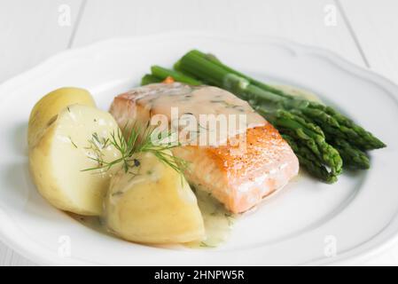 Nahaufnahme von gegrilltes Lachsfilet mit Kartoffeln und Spargel garniert mit Dillsauce auf weiße Platte angeordnet Stockfoto