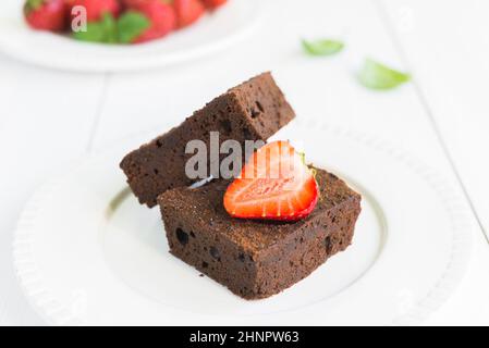 Nahaufnahme von Schokolade-Brownie-Kuchen mit Erdbeeren und auf weißem Teller angeordnet Stockfoto