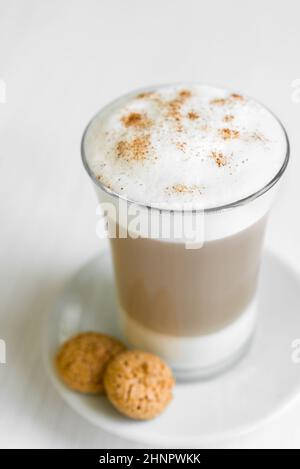 Glas des köstlichen Café Latte mit Biscotti auf weißen Teller und Tisch Stockfoto