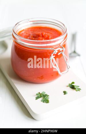 Glas mit frischer hausgemachter Tomatensauce mit Petersilie auf weißer Holztisch angeordnet. Stockfoto
