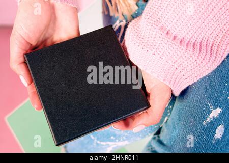 Frauenhände mit pinker Maniküre, die eine schwarze Schachtel hält Stockfoto