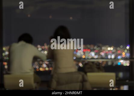Blur paar sitzt auf einem Wolkenkratzer Observatorium mit Blick auf die Nacht der Stadt Stockfoto