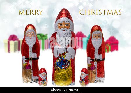 Weihnachtskarte. Nahaufnahme von verschiedenen fröhlich eingewickelten Schokolade Weihnachtsmann über festlichen abstrakten verschwommenen Geschenkschachteln. Inschrift Frohe Weihnachten. Makro. Stockfoto