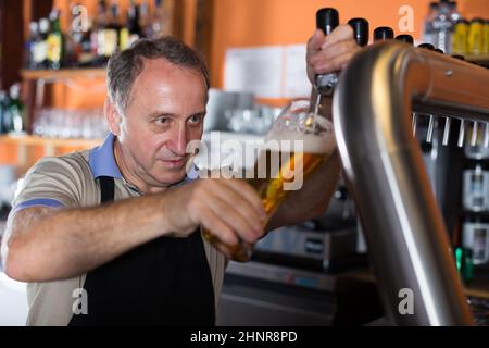 Der lächelnde Barkeeper gießt ungefülltes Bier für den nächsten Gast Stockfoto