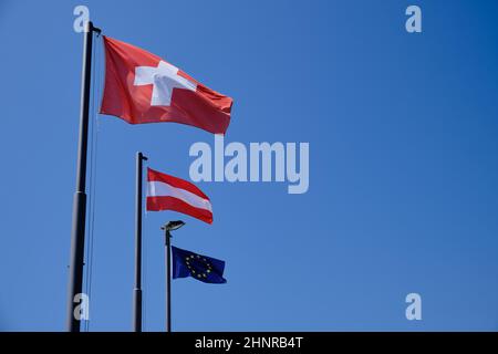Flaggen im Wind der Schweiz, Österreichs und der Europäischen Union mit blauem Himmel im Hintergrund. Stockfoto