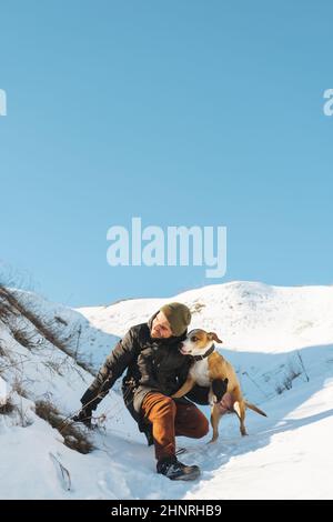 Fröhlicher Mann und sein verspielter Hund, der sich im Schnee auf der sonnigen da amüsieren kann Stockfoto