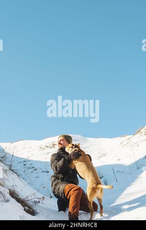 Fröhlicher Mann und sein verspielter Hund, der sich im Schnee auf der sonnigen da amüsieren kann Stockfoto