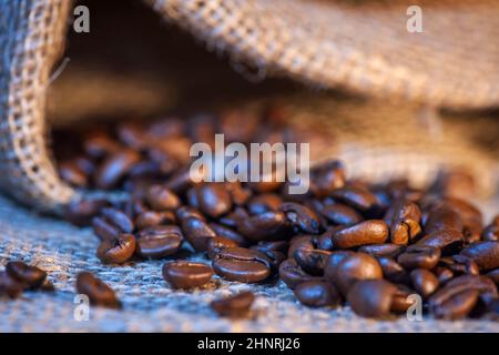 Nahaufnahme von frisch gerösteten Kaffeebohnen, die aus einem Sackleinen gestreut wurden. Stockfoto