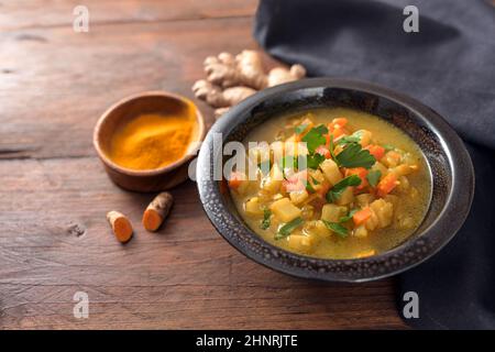 Currsuppe mit Gemüse, Kurkuma und Ingwer in einer dunklen Schüssel auf einem rustikalen Holztisch mit Kopierfläche, ausgewähltem Fokus, enger Schärfentiefe Stockfoto