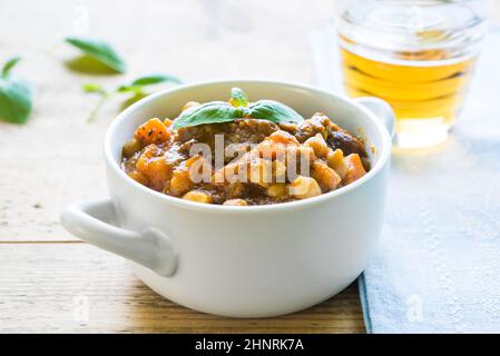 Nahaufnahme von Rindfleisch-Eintopf mit Kichererbsen und Möhren garniert mit frischem Basilikum in einer weißen Schüssel auf einem Holztisch serviert Stockfoto