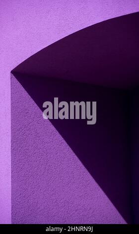 Geometrische schwarze und violette Schattenformen auf der Außenwand des Gebäudes aus Zement oder Beton im Nachmittagslicht, die schwarze Linien trennen Stockfoto