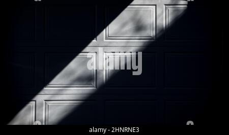 Abstraktes Schwarz-weiß-Design von Schatten und Quadraten auf weißem Garagentor des Hauses in urbaner Umgebung, Lichtstreifen zwischen zwei schwarzen Dreiecken Stockfoto