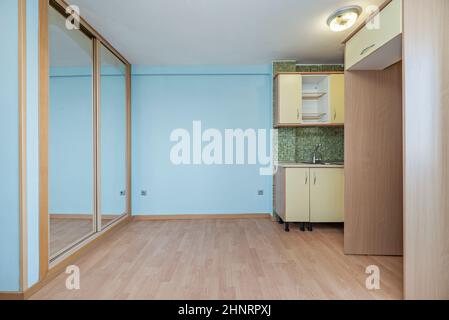 Studio mit einer Eckküche mit einer grün gefliesten Wand und der Rest der Wände hellblau gestrichen und vor der Küche ein Einbauschrank mit Stockfoto